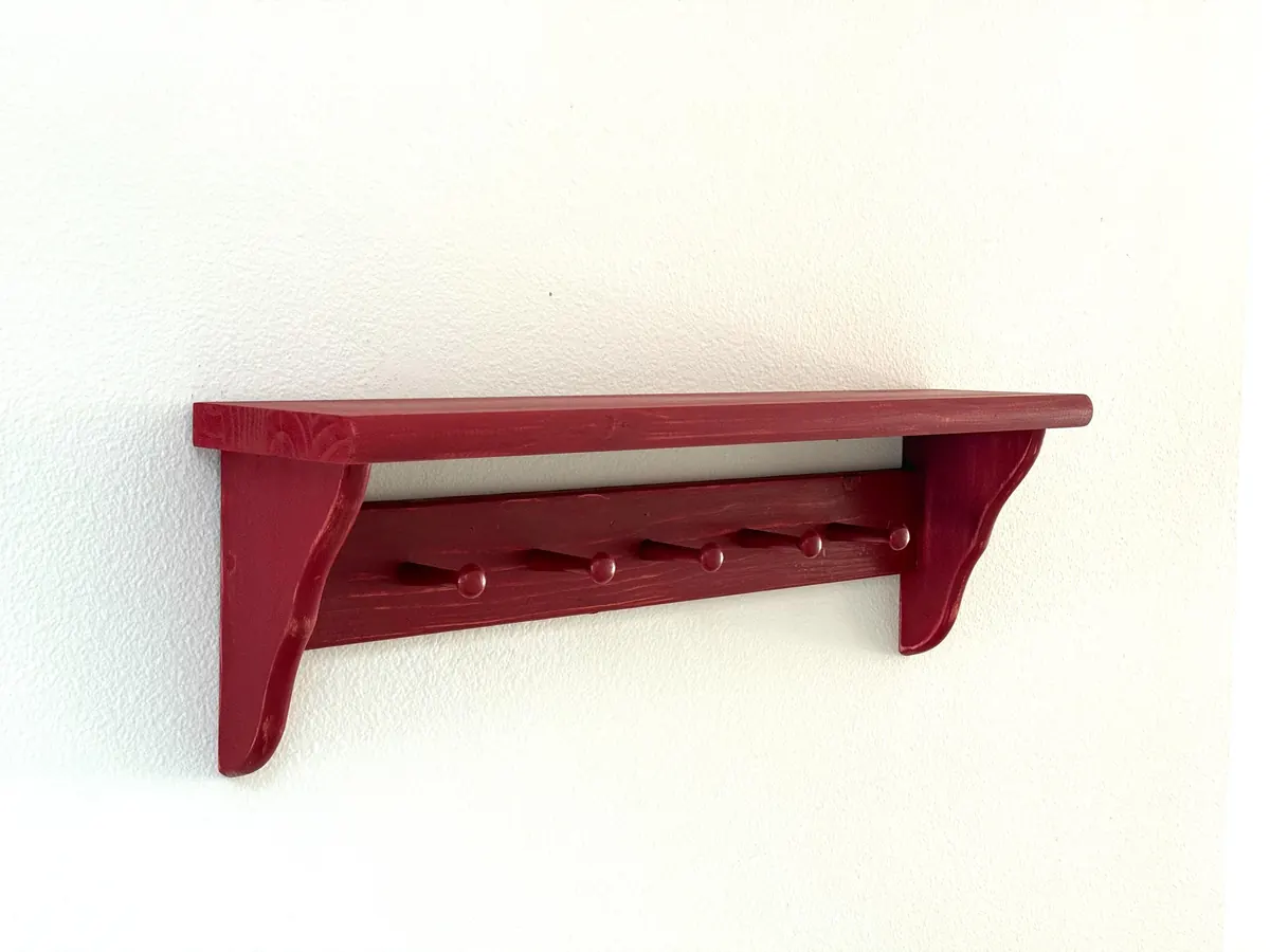 A red-painted Shaker peg shelf with curved brackets on a white wall
