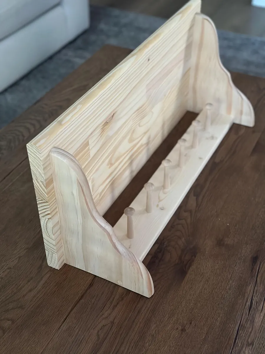 A wide natural pine peg shelf with curved side brackets resting on a wood table