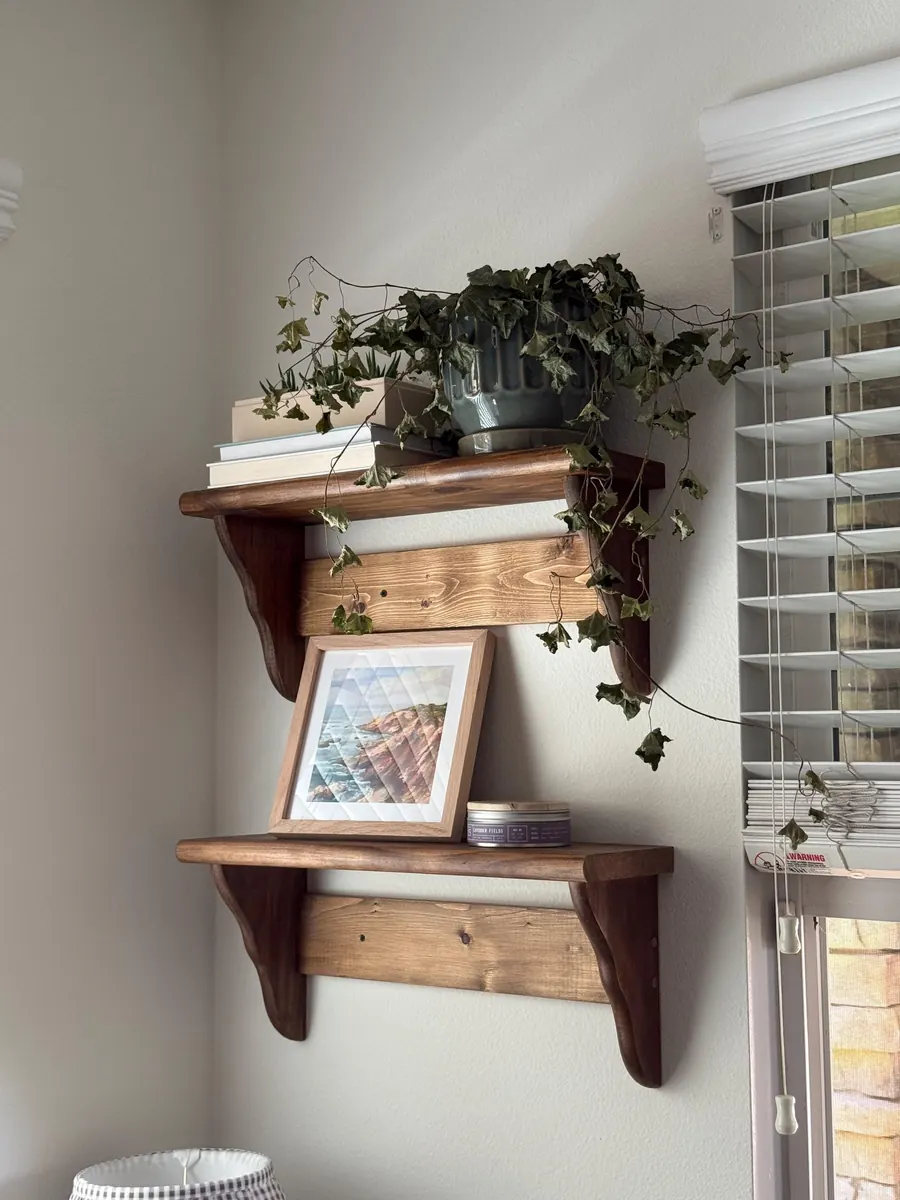 Two stained pine peg shelves stacked on a corner wall with a trailing plant and a framed print