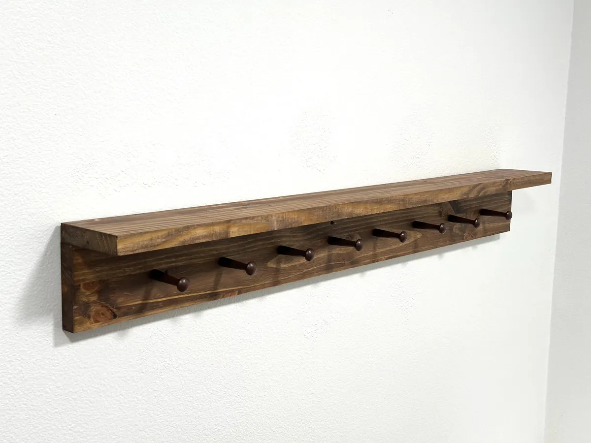 A long stained pine peg shelf with eight wooden pegs on a white wall