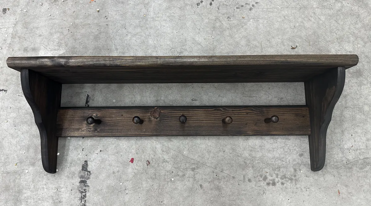 A deep, dark-stained peg shelf with curved brackets and five pegs